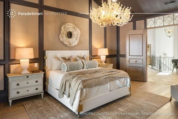 A styled Parade of Homes primary bedroom with an upholstered bed, crystal chandelier, and layered neutral textiles