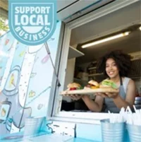 A food truck vendor serving a customer at a Support Local Business booth